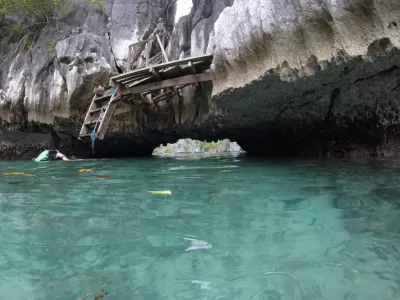 Treoir Taistil Mini: Lá Eachtraíochta i Coron, Palawan : An bealach isteach chuig an murlach i bhfolach, atá frámaithe ag aillte aolchloiche agus fásra lush.