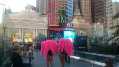 Walking on the best parts of Las Vegas strip up to the neon museum : Nearly naked ladies street performers with feathers on a sky bridge and view on the Big Apple roller coaster